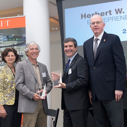 Four people stand together, with two in center holding glass awards.