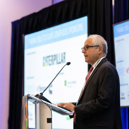 Nabil Nasr presents in front of projector and TV screens.