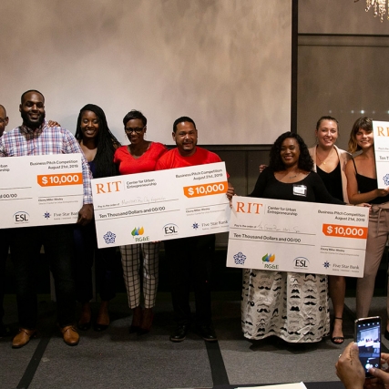 Nine people stand holding four giant novelty checks for $10,000 each.