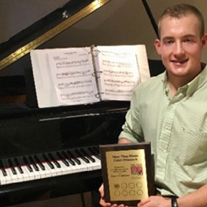 Caleb Wheelock sits in front of his piano with the plaque his nonprofit, More Than Music, earned from the Ride for Missing Children. 