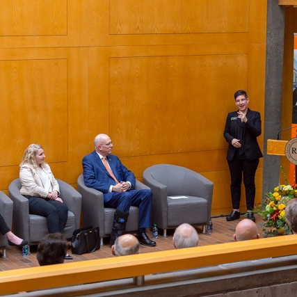 Man speaks at podium with interpreter next to him and three people seated against a wall.