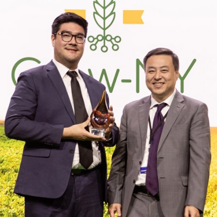 Two businessmen stand holding award.