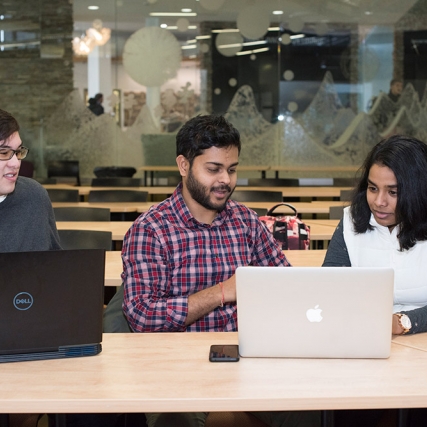 three students at table on laptops.