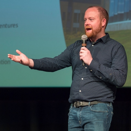 man holding microphone giving presentation on a stage.