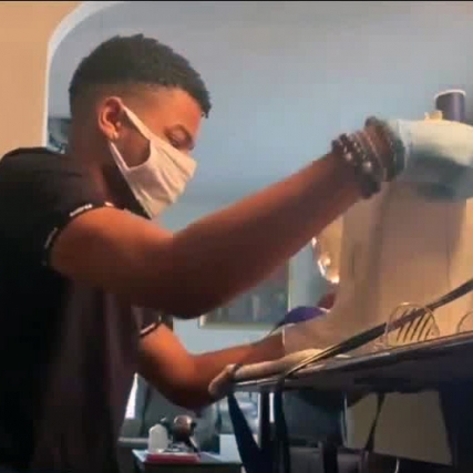 student wearing facemask and gloves operating sewing machine.
