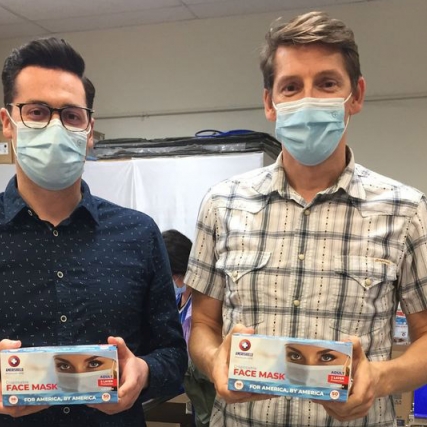 two men wearing disposable fask masks and holding boxes of displosable face masks.
