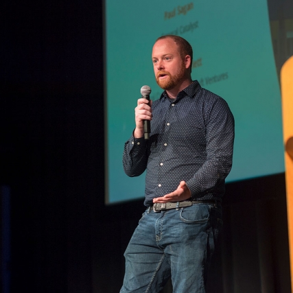 person standing on stage talking into a microphone.
