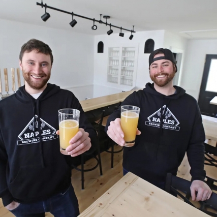 two brewing company owners holding up glasses of beer.