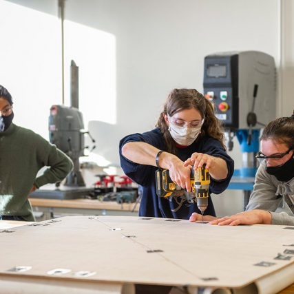 student using a power drill to drill holes into a piece of particle board.