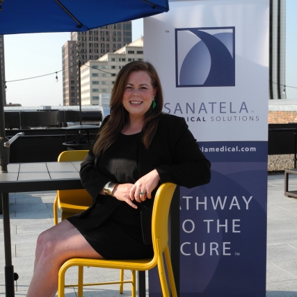 Erin Crowley Ellis sitting at a desk and smiling in front of a sign that says "Sanatela Medical Solutions."