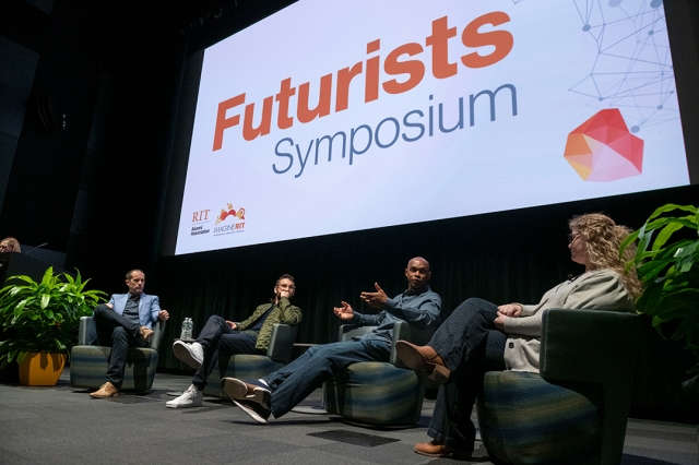 four panelists sit on a stage before a large screen that says, Futurists Symposium.