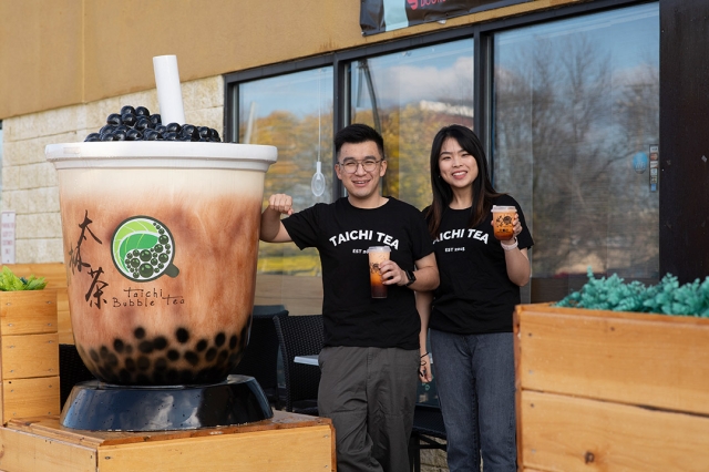 two people holding cups of bubble tea standing outside of the Taichi Bubble Tea store.