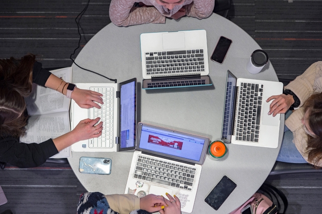 Overhead image of four students at a round table with their laptops in front of them.