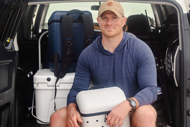 a man sits in the back of an SUV with a white square bag.