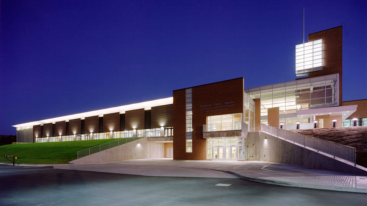 The exterior of the Gordon Field House and Activities Center illuminated at night against a dark blue sky.