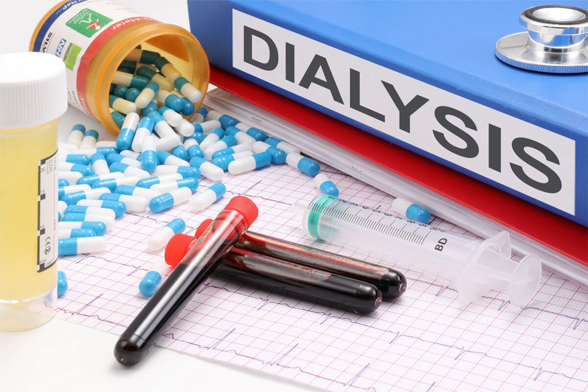 A binder that is labeled with the word dialysis, a pill container spilling out blue and white capsules, three vials of blood, a syringe, and a urine sample.
