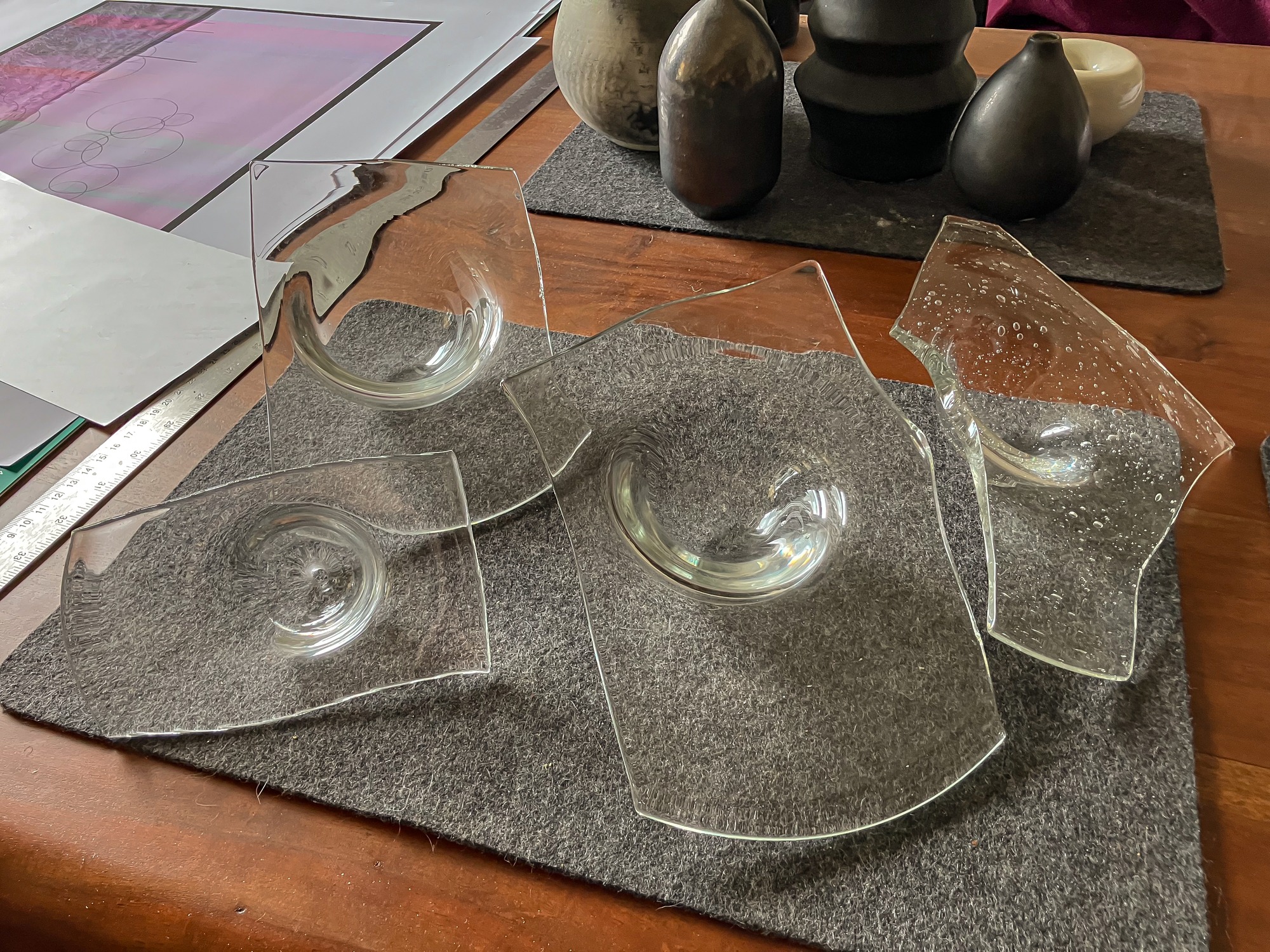 Glass bowl forms with sections removed from their broad rims, arranged on a work surface.