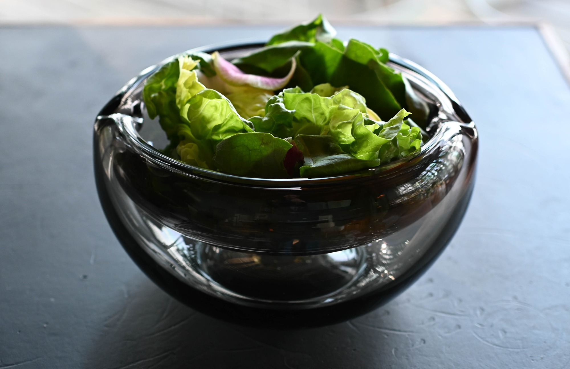 Notched glass bowl holding salad leaves.