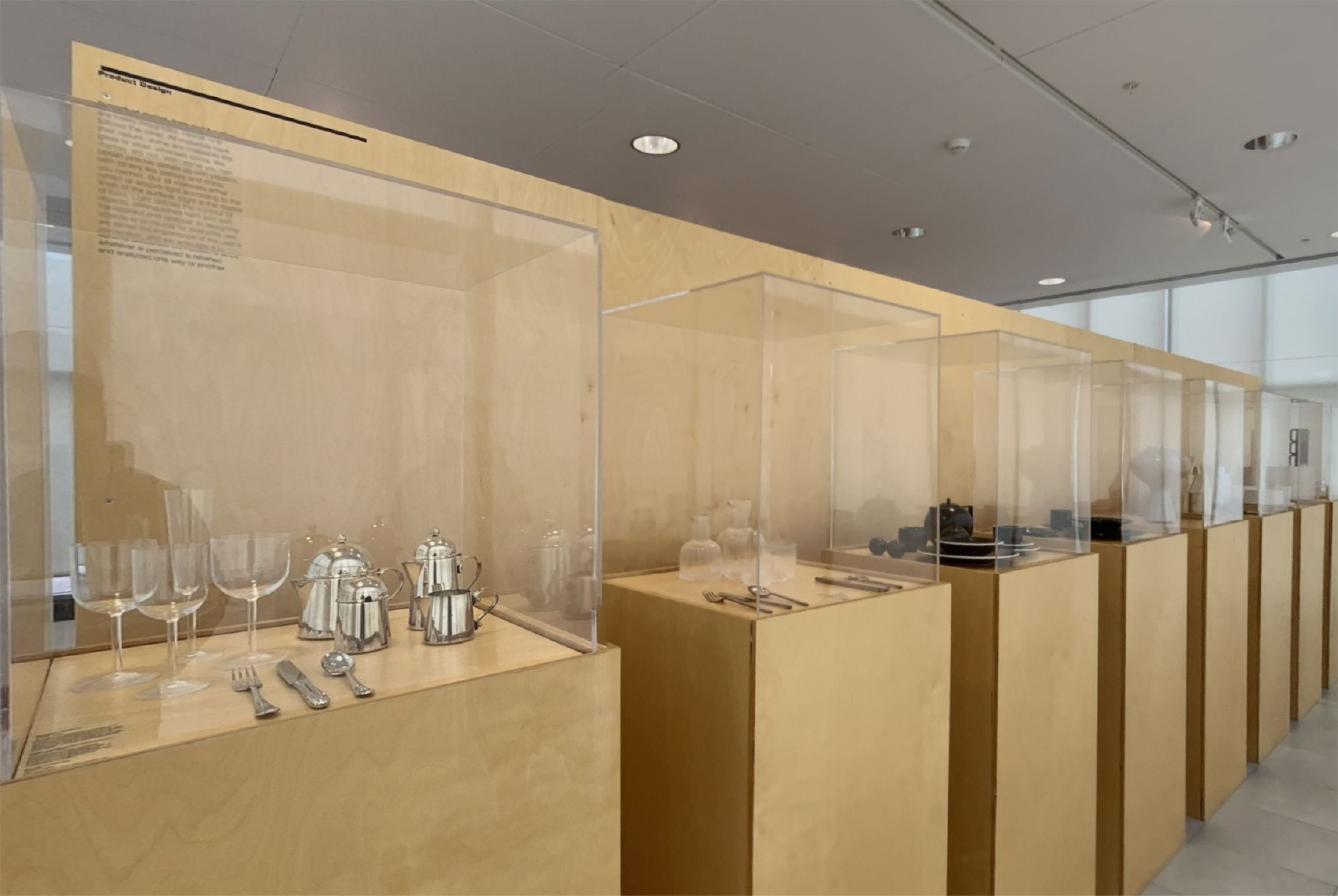 Display cases on wooden pedestals showcasing elegant glassware and silver teapots in an exhibition.