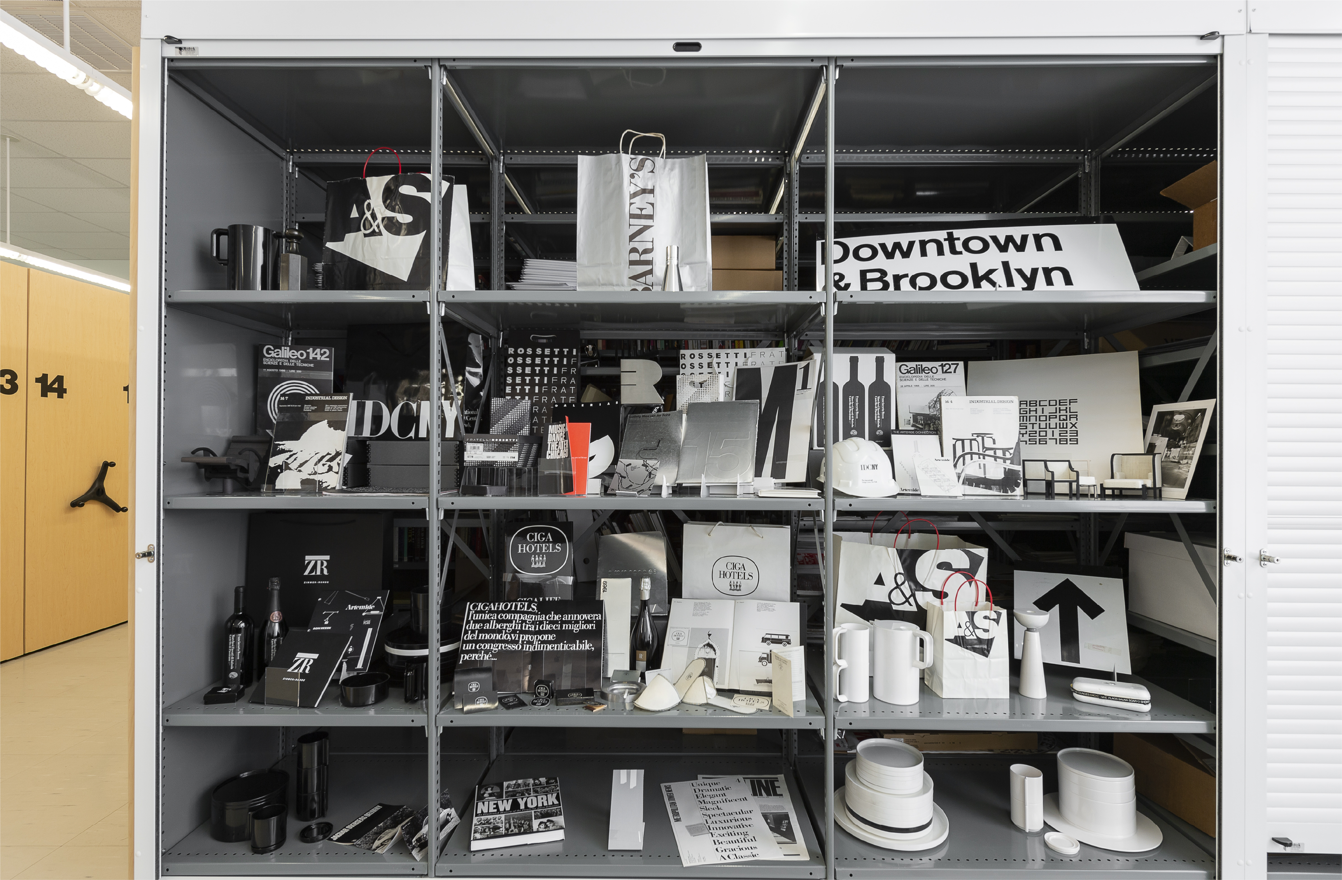 Metal storage shelves in a room filled with various monochromatic design items and printed materials.