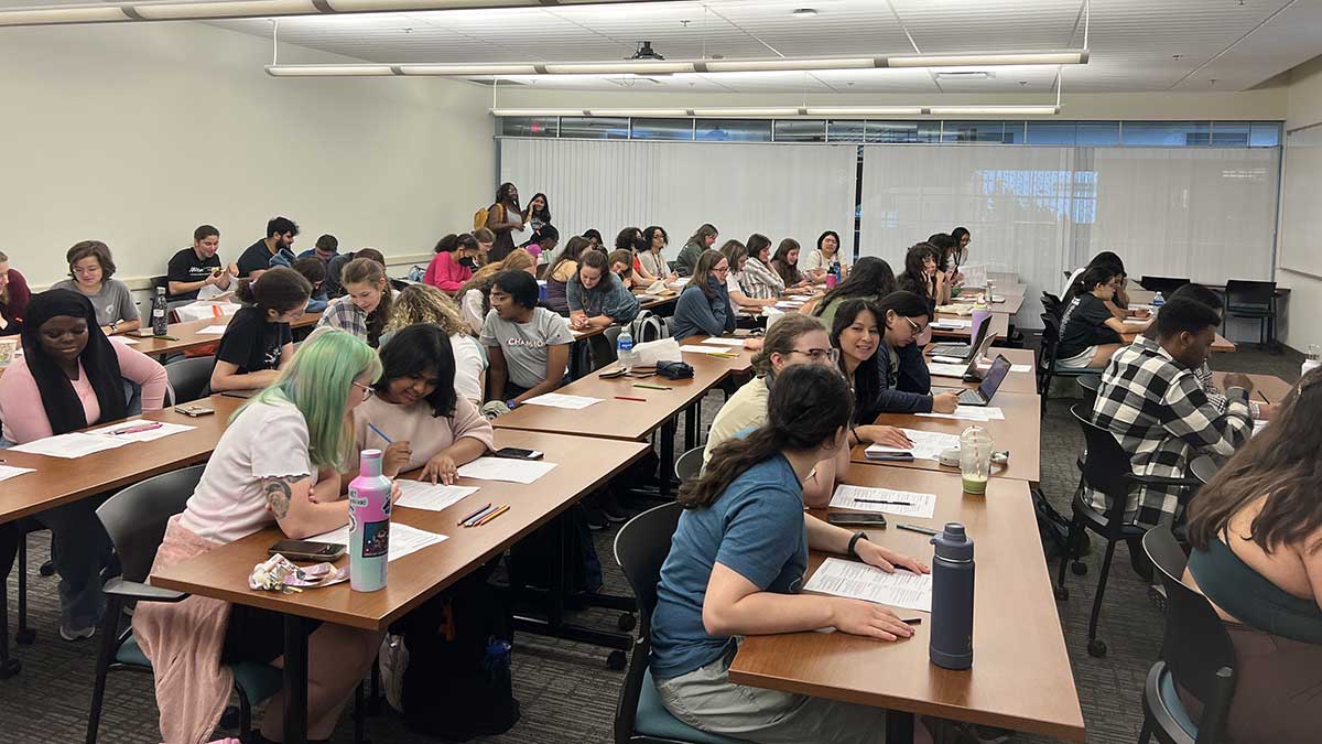A classroom filled with students working together at long tables on written activities.