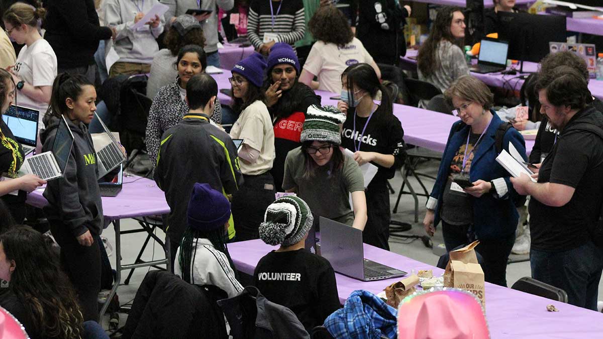 A crowded event space with students collaborating on laptops during a hackathon.