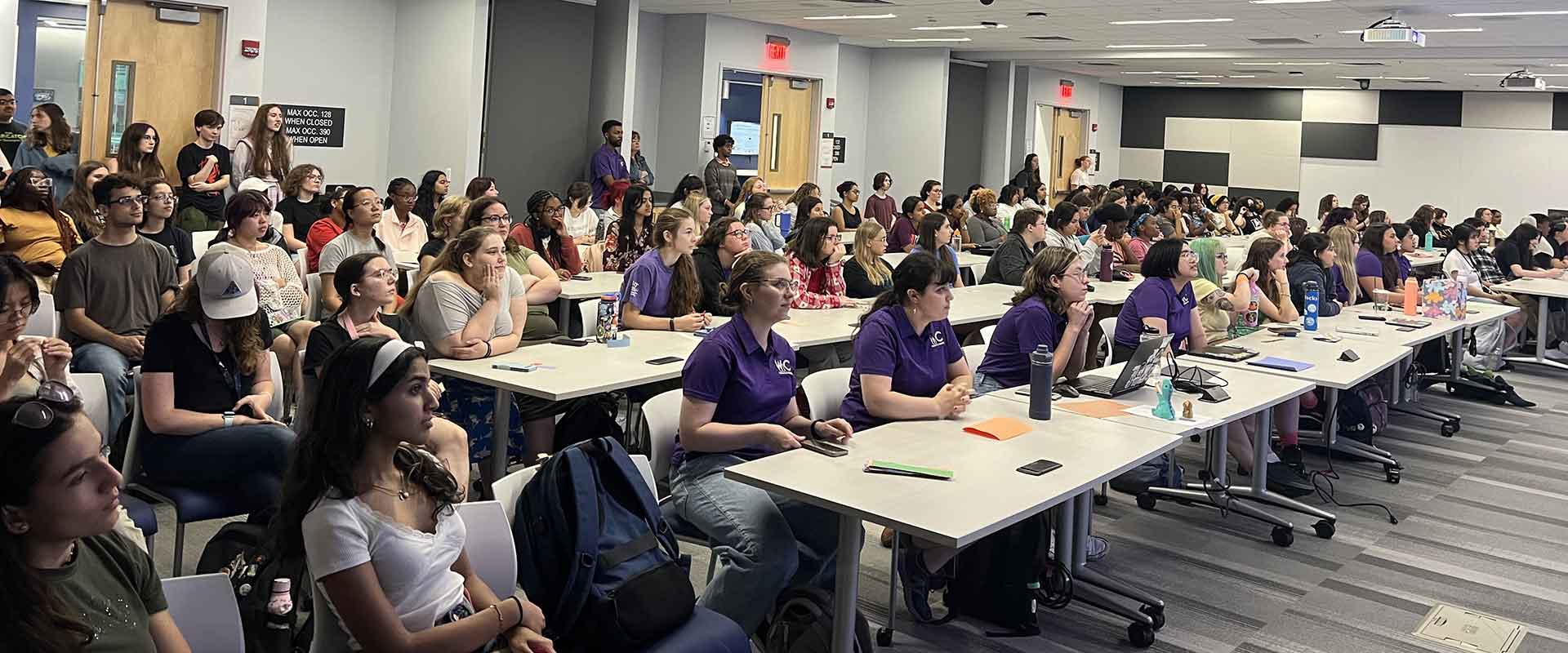 A large audience of students attentively listens to a lecture in a modern classroom.