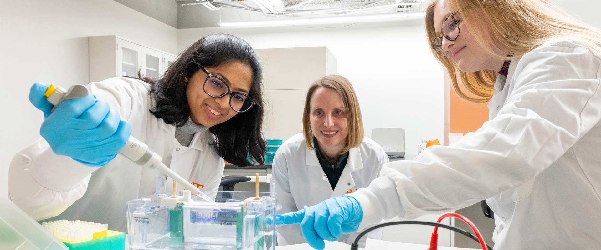 a researcher watches two students in a lab use a pippette.