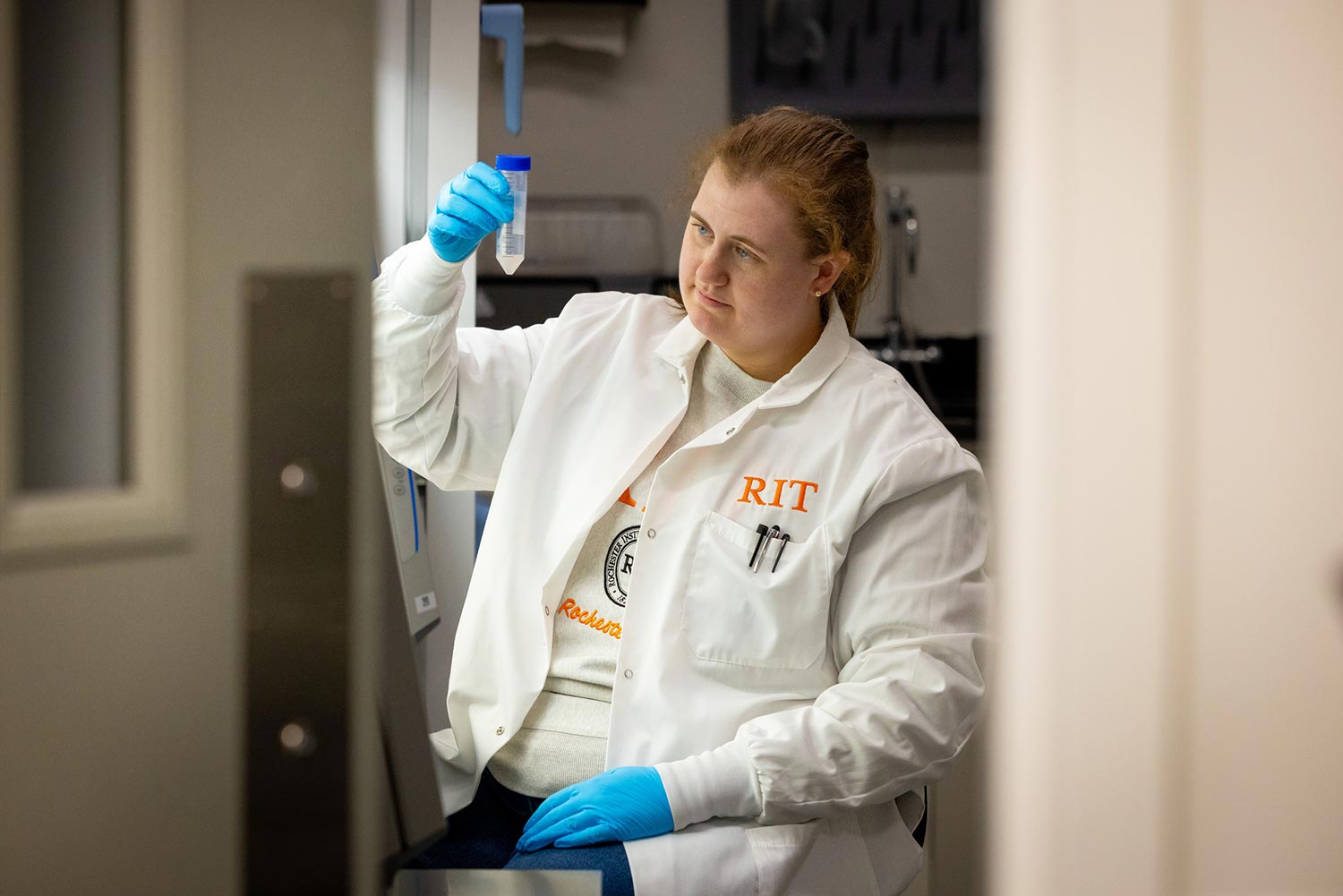 student researcher holds a tube up and looks at the contents.
