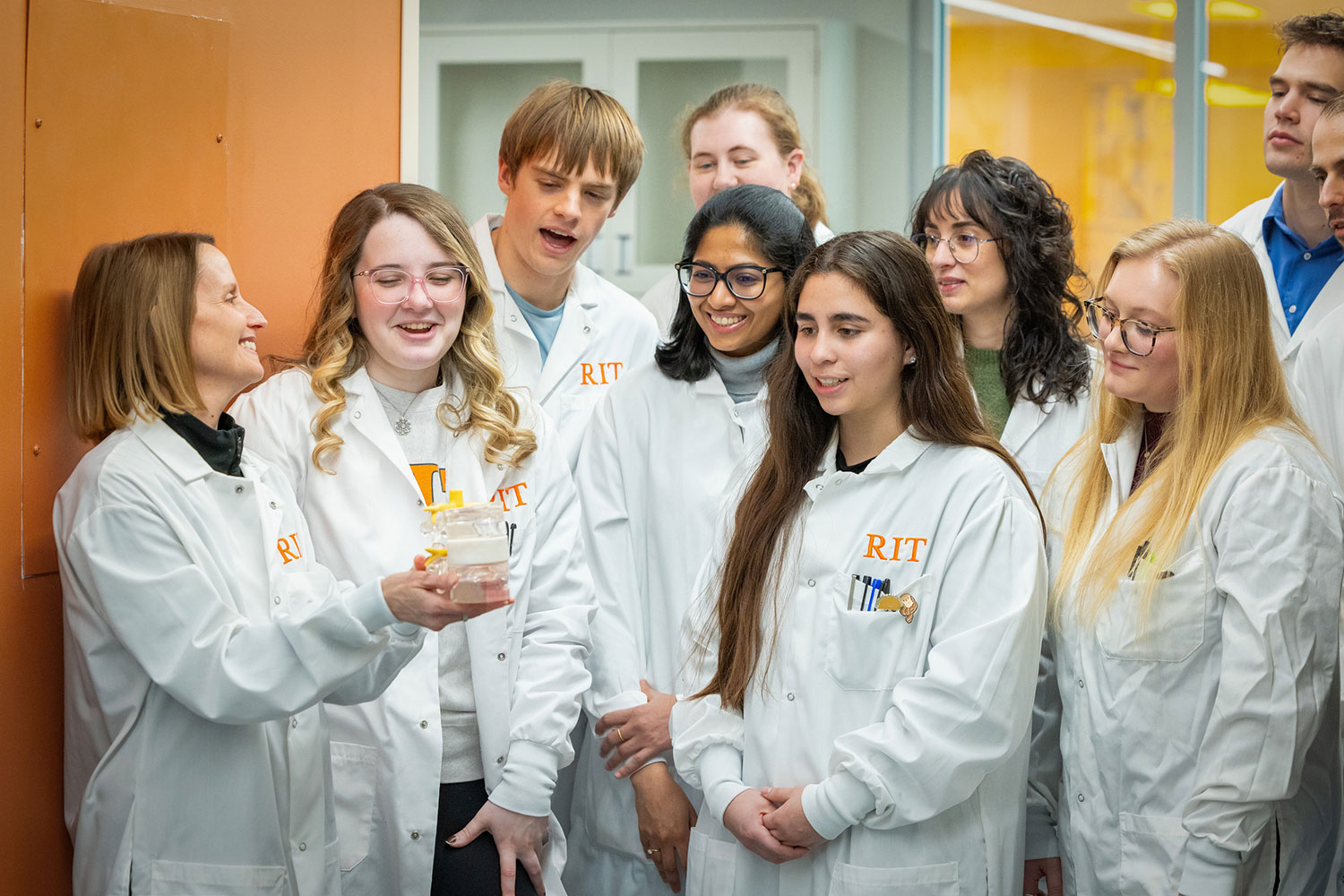 group of student researchers looks at lead researcher holding a jar.