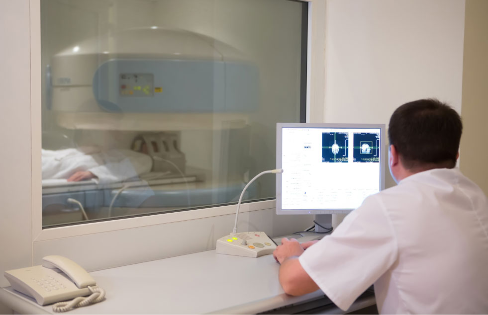 doctor analyzing results on a computer while a patient is in a imaging machine.