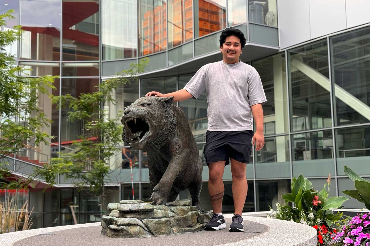 student posing with the R I T tiger statue.