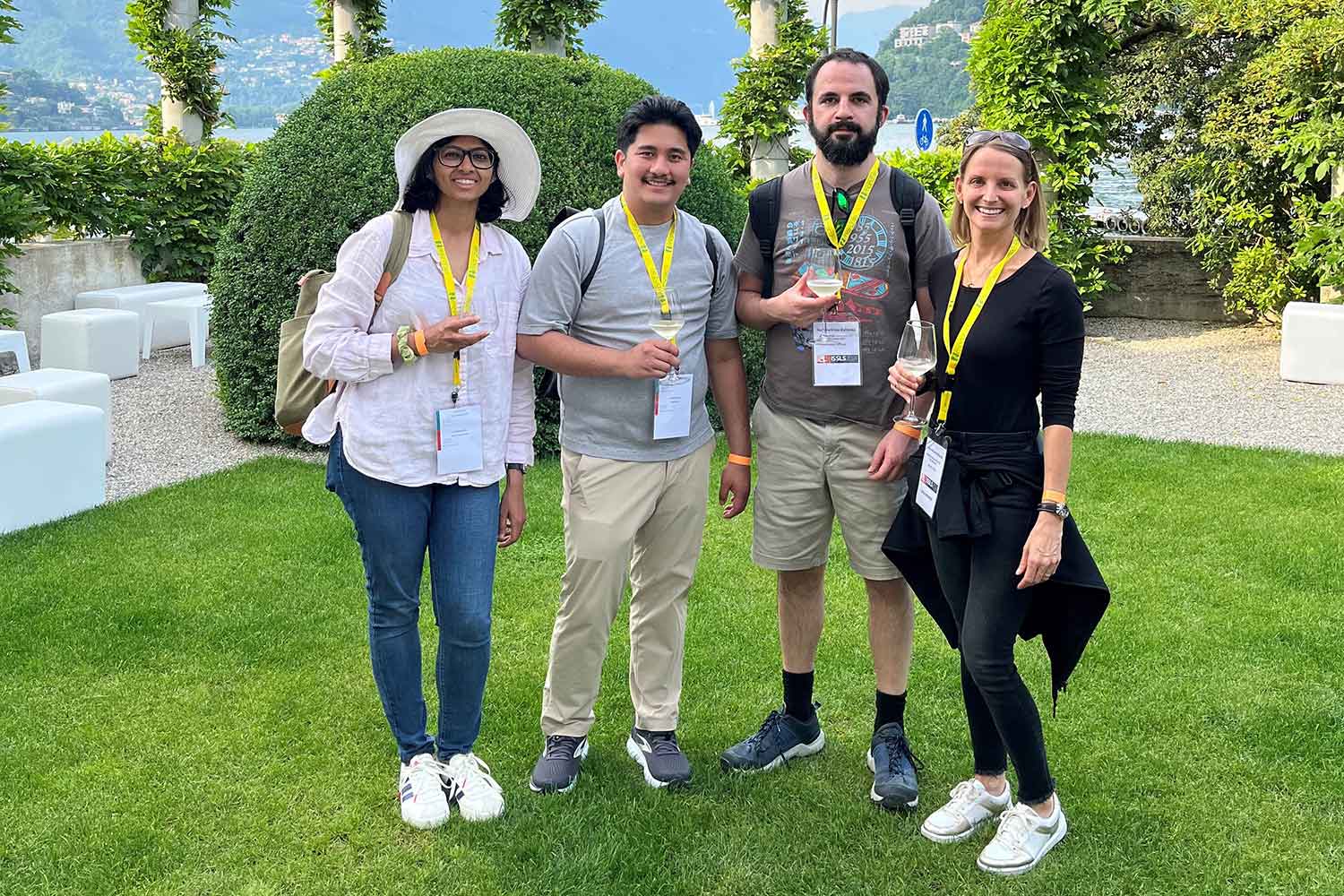 four people posing for a photo outdoors in a well manicured garden.