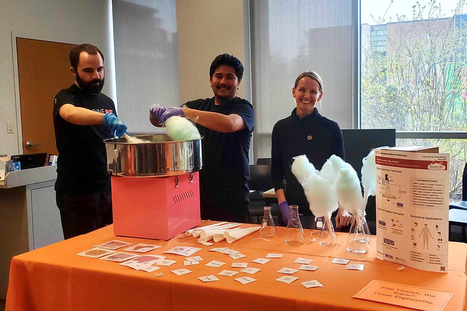 three people making cotton candy at a table.