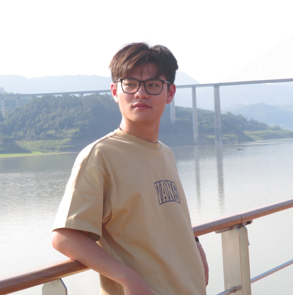 Portrait of Han standing outdoors by water and mountains.