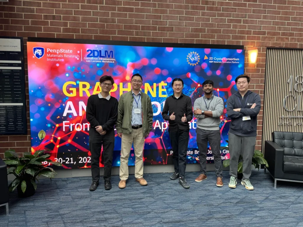 Xu Group members standing together in front of the Graphene and Beyond conference display.