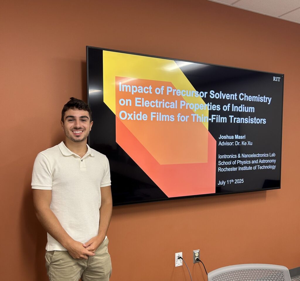 Josh standing beside a display screen showing his M.S. thesis defense title slide.