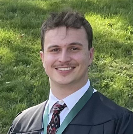 Ben Crocker smiling outdoors in graduation attire with a green stole.