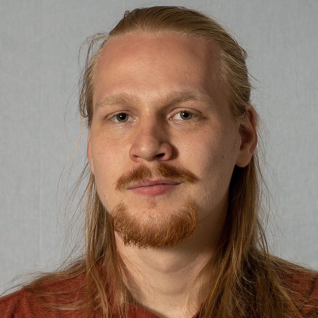 Caleb Bush facing the camera in a close portrait against a plain gray background.