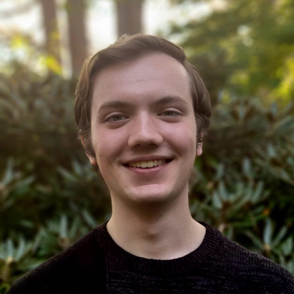 Jacob Eisensmith smiling outdoors with greenery in the background.
