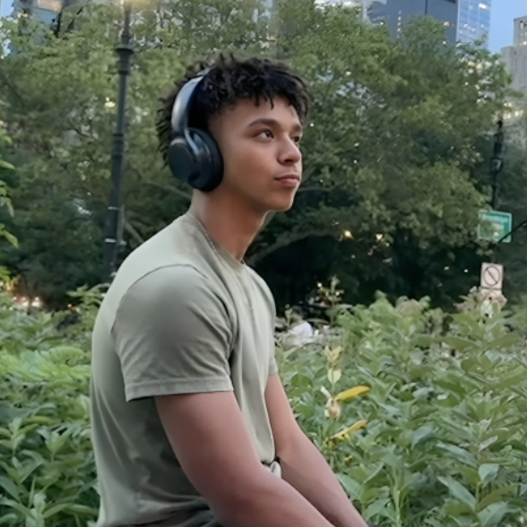 Joniel Yege sitting outdoors in a park setting while wearing over-ear headphones.