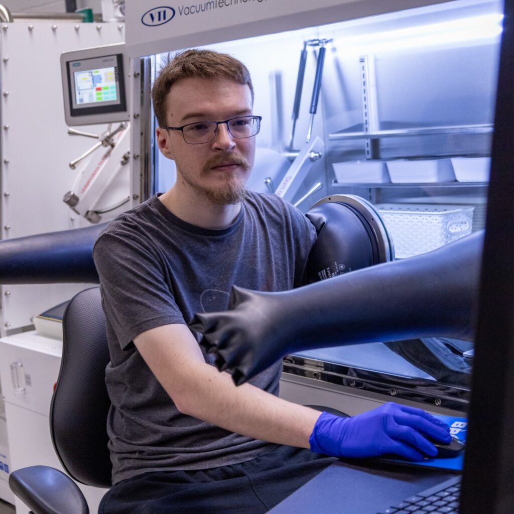 Wyatt Morrell working at a laboratory glovebox while wearing blue gloves.